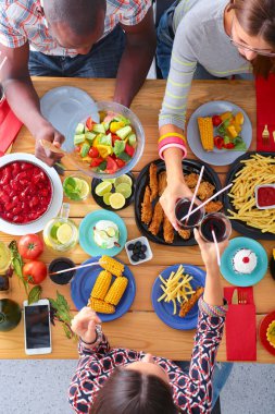 Ahşap masada otururken birlikte yemek yiyen bir grup insanın üst düzey görüntüsü. Masada yemek var. İnsanlar fast food yiyor..