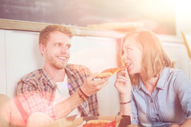 Genç çift, yeni bir eve taşındıktan sonra etraflarında kutularla yerde pizza molası veriyorlar. Genç çift