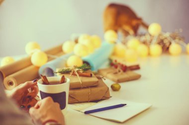 Noel hediye kutusu ile masaya oturan kadın. Kadının elleri