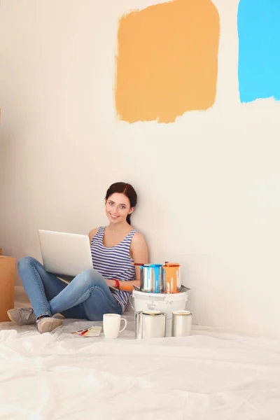 Ritratto di giovane donna mentre dipinge un nuovo appartamento, seduta con computer portatile. Giovane donna con computer portatile — Foto Stock