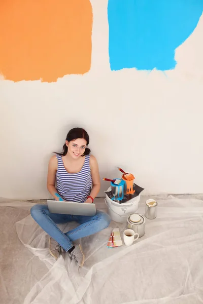 Πορτρέτο της νεαρής γυναίκας ενώ ζωγραφική νέο διαμέρισμα, κάθονται με το laptop. Νεαρή γυναίκα με φορητό υπολογιστή — Φωτογραφία Αρχείου