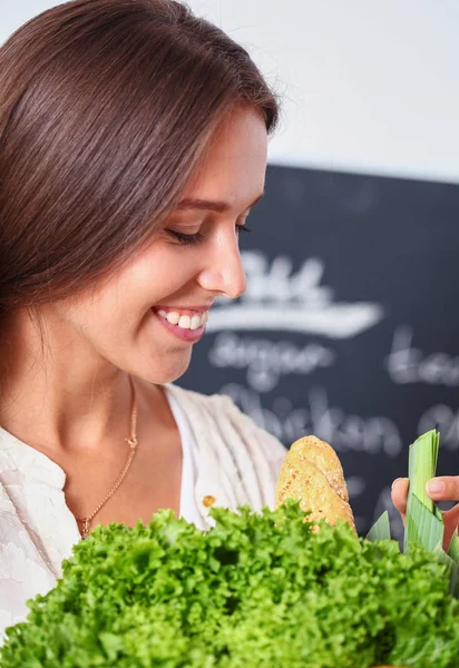 Mujer joven sonriente sosteniendo verduras de pie en la cocina. Jovencita sonriente —  Fotos de Stock