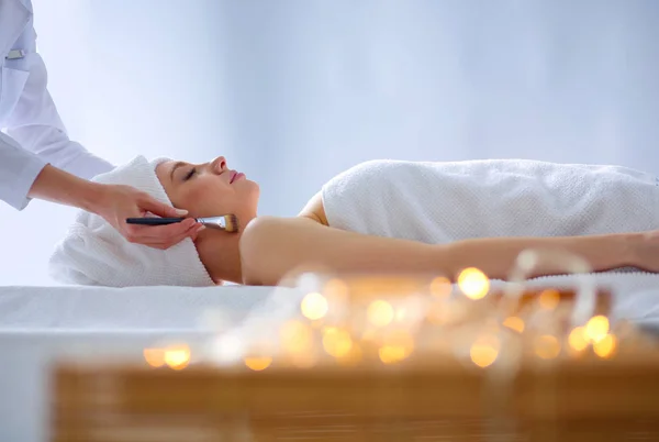 Mujer joven acostada en una mesa de masaje, relajándose con los ojos cerrados. Una mujer. Salón de spa —  Fotos de Stock