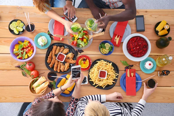 Widok z góry na grupę ludzi jedzących razem kolację siedząc przy drewnianym stole. Jedzenie na stole. Ludzie jedzą fast food. — Zdjęcie stockowe
