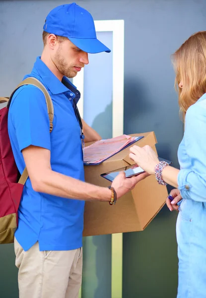 Repartidor sonriente con uniforme azul que entrega la caja de paquetes al destinatario: concepto de servicio de mensajería. Repartidor sonriente en uniforme azul — Foto de Stock