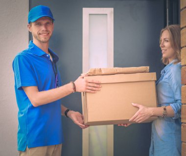 Mavi üniformalı gülümseyen kurye servis konseptine paket kutusu teslim eden teslimatçı. Mavi üniformalı gülümseyen teslimatçı.