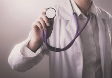 Genç bir bayan doktor dinliyor, elinde tıbbi steteskop var.