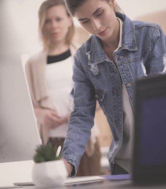 Masanın yanında duran iki genç kadın enstrüman, plan ve dizüstü bilgisayarla