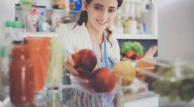 Sağlıklı yiyecek, sebze ve meyvelerle dolu açık buzdolabının yanında duran kadın portresi. Kadın portresi