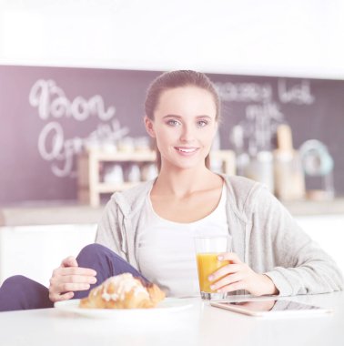 Mutfakta portakal suyu ve tableti olan genç bir kadın..