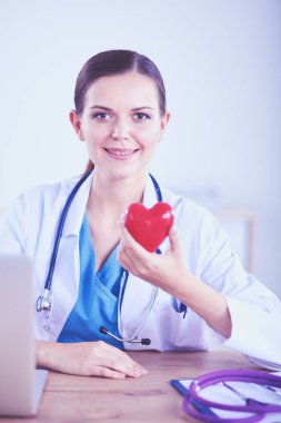 Masada oturan ve kalp tutan güzel genç gülümseyen kadın doktor.