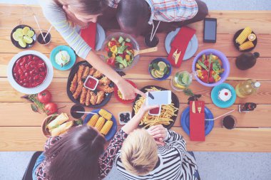 Ahşap masada otururken birlikte yemek yiyen bir grup insanın üst düzey görüntüsü. Masada yemek var. İnsanlar fast food yiyor..