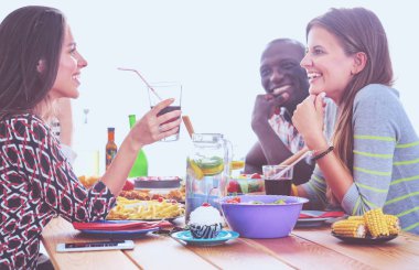 Ahşap masada otururken birlikte yemek yiyen bir grup insanın üst düzey görüntüsü. Masada yemek var. İnsanlar fast food yiyor..