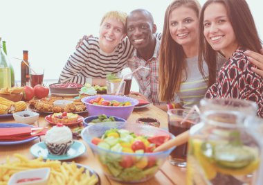 Ahşap masada otururken birlikte yemek yiyen bir grup insanın üst düzey görüntüsü. Masada yemek var. İnsanlar fast food yiyor..