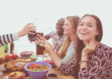 Ahşap masada otururken birlikte yemek yiyen bir grup insanın üst düzey görüntüsü. Masada yemek var. İnsanlar fast food yiyor.