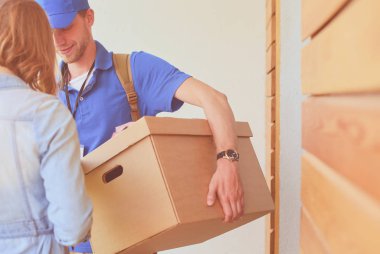Mavi üniformalı gülümseyen kurye servis konseptine paket kutusu teslim eden teslimatçı. Mavi üniformalı gülümseyen teslimatçı.
