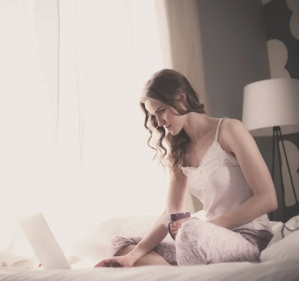 Νεαρή όμορφη γυναίκα που κάθεται στο κρεβάτι με το lap-top. — Φωτογραφία Αρχείου