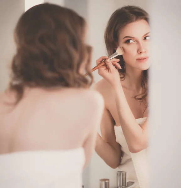 Jonge vrouw kijken in de spiegel en zetten make-up op. — Stockfoto