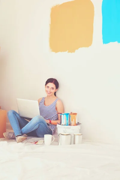 Portret van de jonge vrouw tijdens het schilderen van nieuw appartement, zitten met laptop. Jonge vrouw met laptop — Stockfoto
