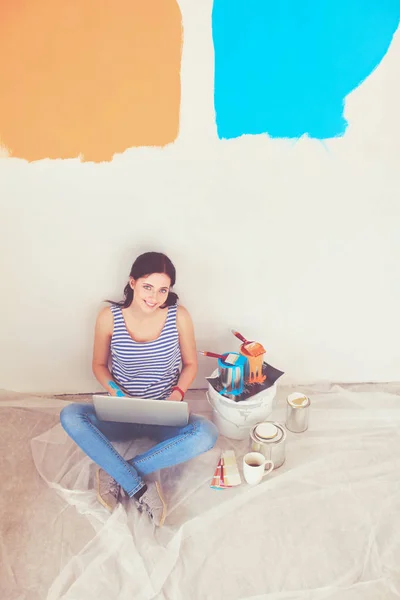 Portret van de jonge vrouw tijdens het schilderen van nieuw appartement, zitten met laptop. Jonge vrouw met laptop — Stockfoto