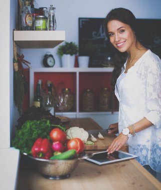 Mutfakta yemek yapmak için tablet bilgisayar kullanan genç bir kadın.