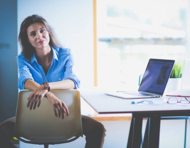 Ofis masasında dizüstü bilgisayarla oturan genç bir kadın. Genç bir kadın. Dizüstü bilgisayar