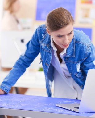 Masanın yanında duran iki genç kadın enstrüman, plan ve dizüstü bilgisayarla.