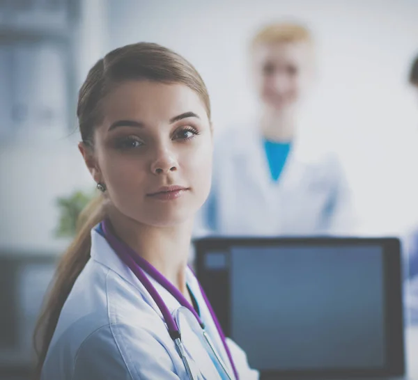 Schöne junge lächelnde Ärztin sitzt am Schreibtisch — Stockfoto