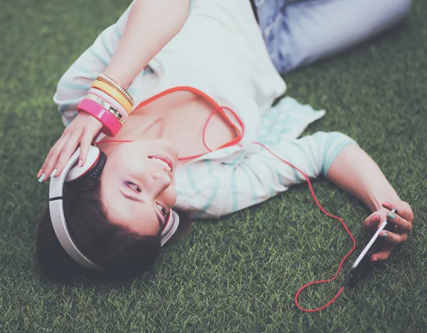 Žena poslechu hudby leží na zelené trávě — Stock fotografie
