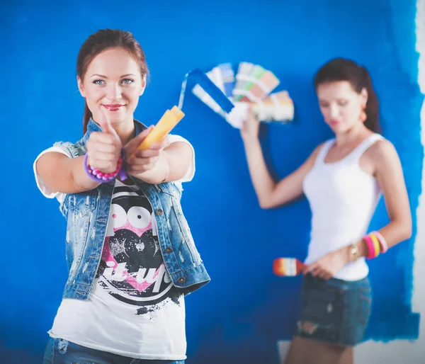 Dos hermosas mujeres jóvenes sosteniendo la paleta de colores, de pie cerca de la pared. Dos mujeres hermosas jóvenes — Foto de Stock