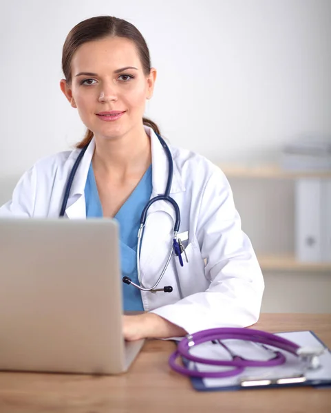 Hermosa joven sonriente doctora sentada en el escritorio y escribiendo — Foto de Stock