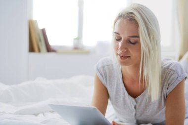 Elinde boş ekranlı dijital tablet tutan ve yatak odasında kameraya gülümseyen bir kız.