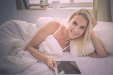 Elinde boş ekranlı dijital tablet tutan ve yatak odasında kameraya gülümseyen bir kız.