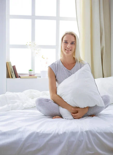Cute woman holding a pillow while sitting on her bed — Stock Photo, Image