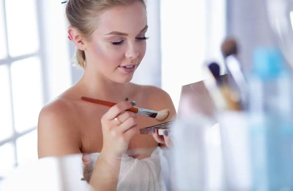 Una foto de una mujer joven aplicando polvo facial en el baño —  Fotos de Stock