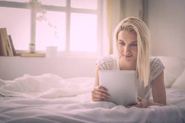 Chica sosteniendo tableta digital con pantalla en blanco y sonriendo a la cámara en el dormitorio — Foto de Stock