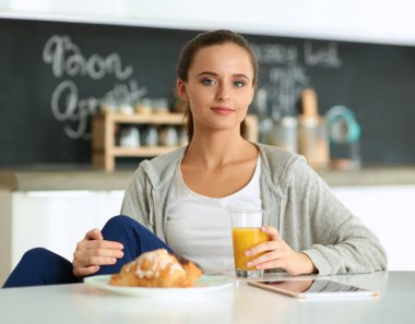 Mutfakta portakal suyu ve tableti olan genç bir kadın.