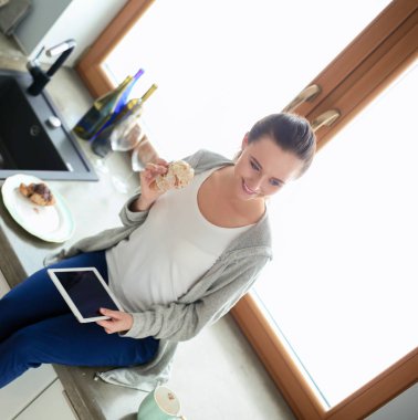 Mutfakta dijital tablet kullanan güzel genç bir kadın..