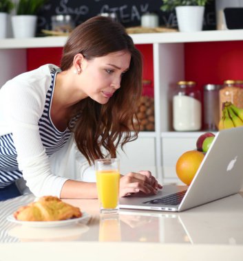 Dizüstü bilgisayar kullanarak ve mutfakta oturmuş çekici genç kadın