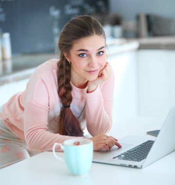 Mutfakta dizüstü bilgisayar kullanan genç bir kadın.