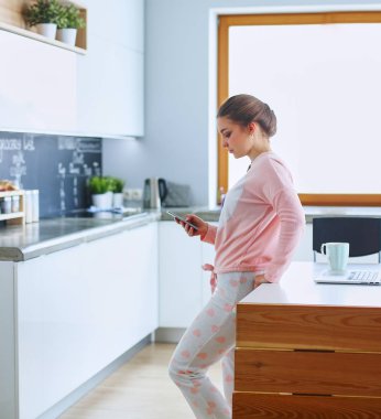 Cep telefonu ayakta modern mutfak kullanan kadın