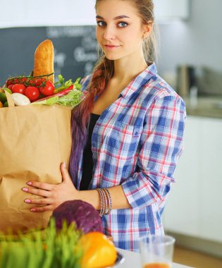 Elinde sebzeli alışveriş torbası tutan genç bir kadın.