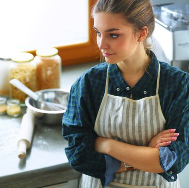 Güzel bir kadın mutfakta pasta pişiriyor. Masanın yanında duruyor.