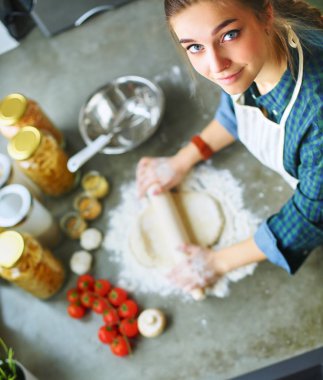 Güzel bir kadın mutfakta pasta pişiriyor. Masanın yanında duruyor.