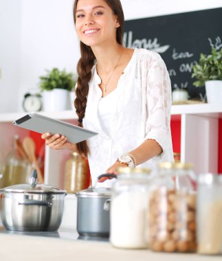 Mutfakta yemek yapmak için tablet bilgisayar kullanan genç bir kadın.