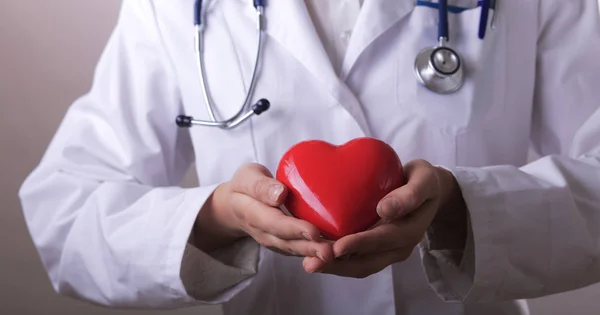 Médecin femme avec stéthoscope tenant le cœur, sur fond sombre — Photo