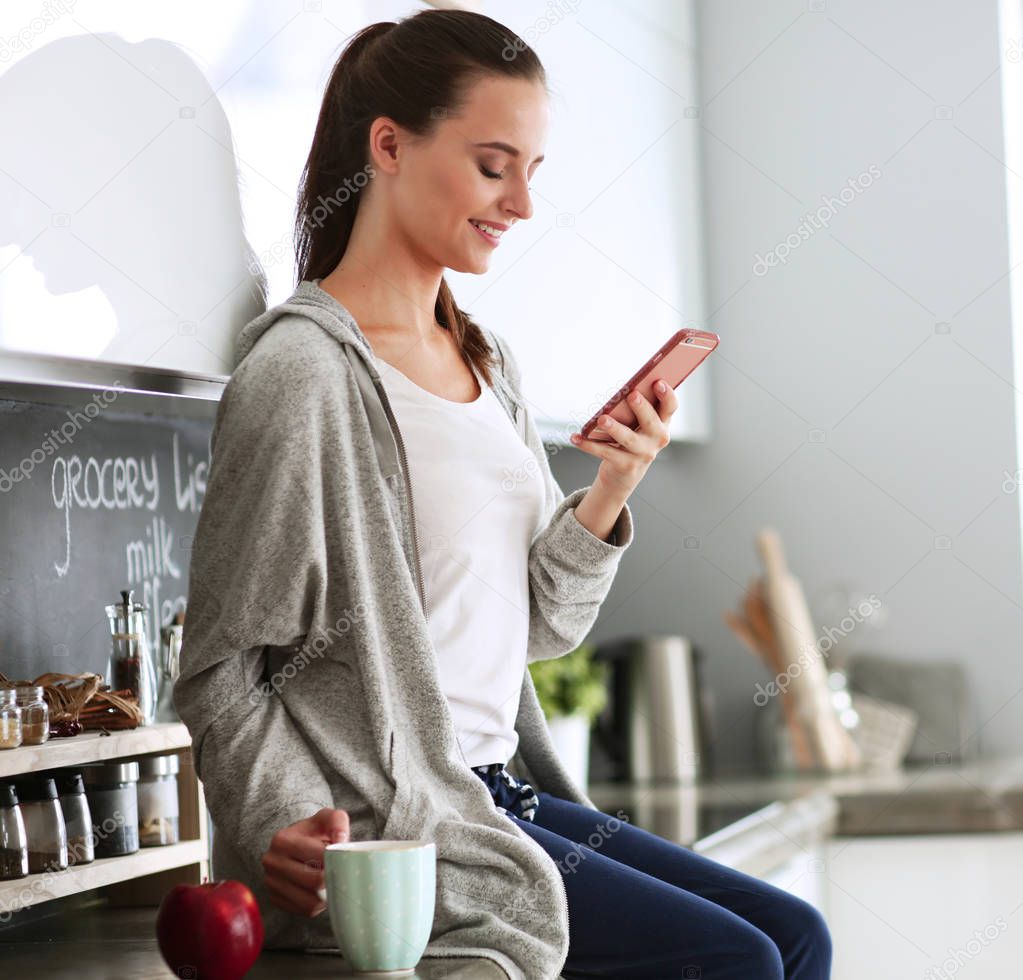 Woman using mobile phone sitting in modern kitchen