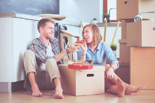 젊은 부부는 피자 점심 그들 주위의 상자를 가진 새로운 가정으로 움직이기 후에 바닥에 휴식. 젊은 커플 — 스톡 사진