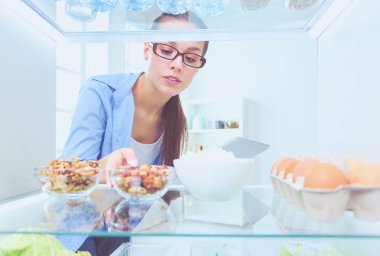 Sağlıklı yiyecek, sebze ve meyvelerle dolu açık buzdolabının yanında duran kadın portresi..