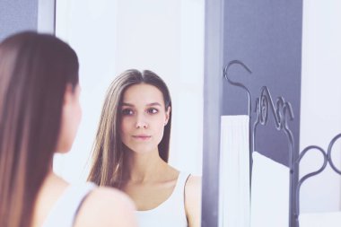 Genç kadın kendini evde aynada yansıma arıyor.